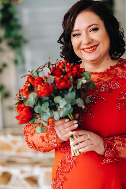 Una donna con un vestito rosso sta in piedi e tiene un mazzo di rose rosse e fragole all'interno.