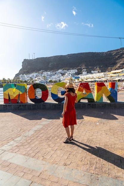 Una donna con un vestito rosso sul cartello turistico nella città costiera di Mogan nel sud di Gran Canaria, in Spagna