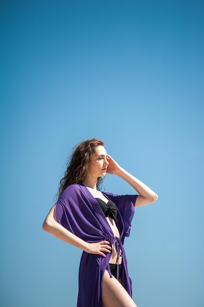 Una donna con un vestito viola si trova di fronte a un cielo blu.
