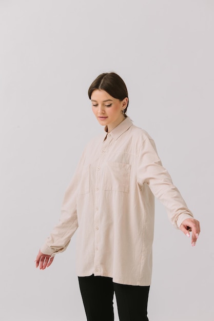 Una donna con una camicia beige sta facendo yoga davanti a uno sfondo bianco