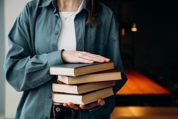 Una donna con una camicia blu tiene una pila di libri su uno sfondo scuro della biblioteca