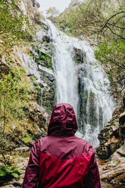 Una donna con una cerata viola in piedi davanti a una cascata gigante