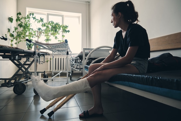 una donna con una gamba rotta si siede su un divano d'ospedale e guarda fuori dalla finestra ferita alla gamba