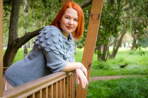 una donna con una gonna e un maglione lavorato a maglia si trova sulla terrazza in legno della sua casa di campagna