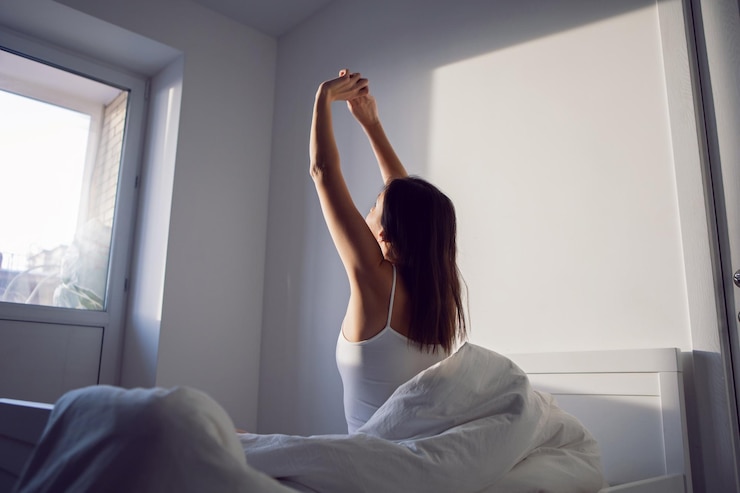 Foto una donna con una maglietta bianca è seduta sul letto sotto la coperta nella stanza al mattino