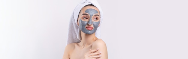 Una donna con una maschera cosmetica in argilla grigia in un asciugamano bianco sulla testa su sfondo bianco