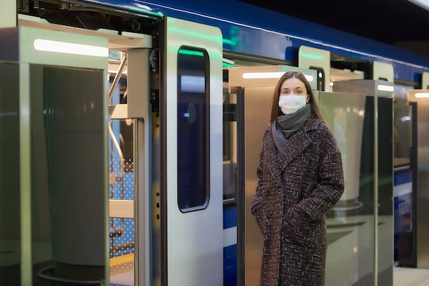 Una donna con una maschera medica per evitare la diffusione del coronavirus sta aspettando vicino al moderno vagone della metropolitana