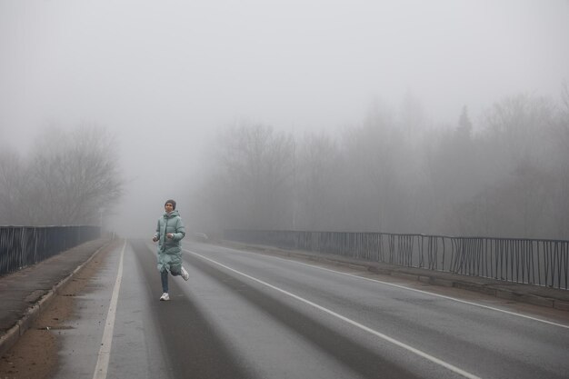 Una donna corre lungo una strada nebbiosa su una strada nebbiosa di una giornata autunnale