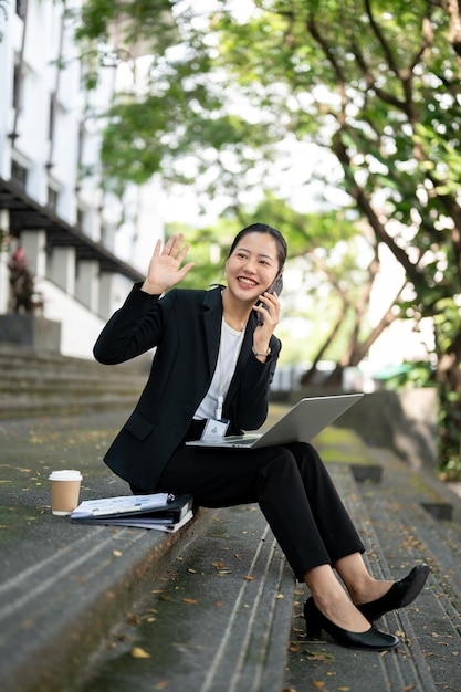 Una donna d'affari asiatica allegra agita la mano mentre parla al telefono sulle scale
