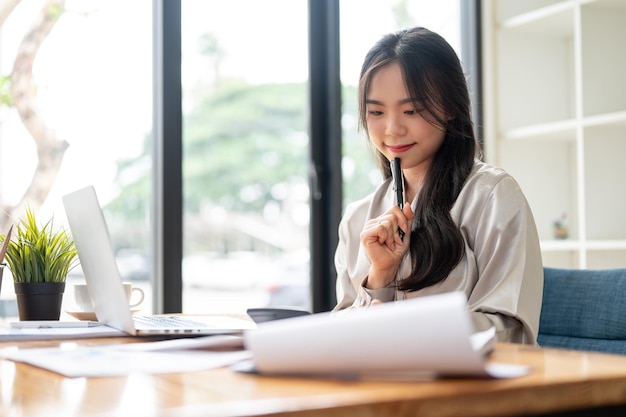 Una donna d'affari asiatica bella e professionale si sta concentrando sul suo lavoro alla sua scrivania in ufficio