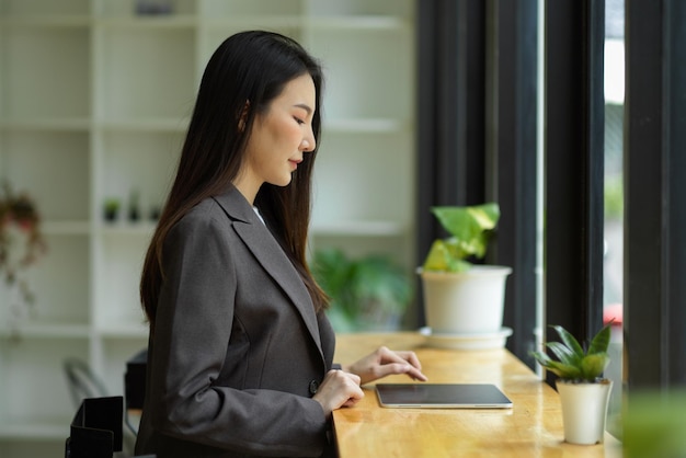 Una donna d'affari asiatica di successo e intelligente in abito formale si siede al bar durante la pausa pranzo e lavora sul suo tablet digitale.