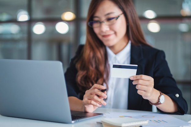 Una donna d'affari asiatica in possesso di carte di credito mentre utilizza il computer portatile in ufficio