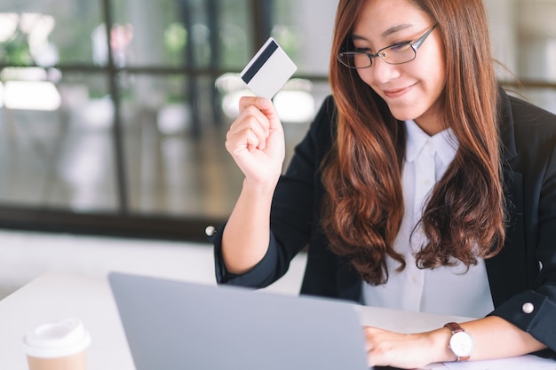 Una donna d'affari asiatica in possesso di carte di credito mentre utilizza il computer portatile in ufficio