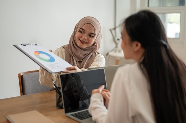 Una donna d'affari asiatica-musulmana sta discutendo di lavoro e facendo brainstorming su un progetto con il suo collega