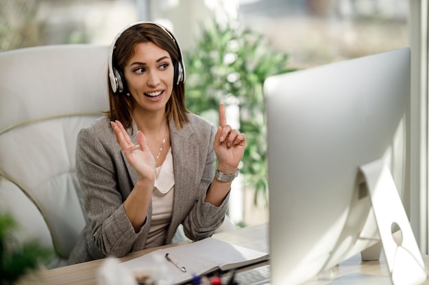 Una donna d'affari attraente con le cuffie e l'utilizzo di un computer per tenere una conferenza web in ufficio a casa.