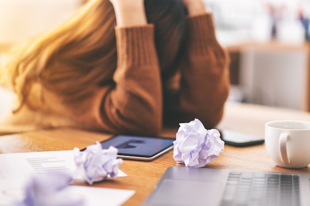 Una donna d'affari che lavora sentendosi frustrata e stressata con documenti e laptop rovinati sul tavolo in ufficio
