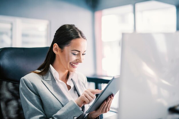 Una donna d'affari che scorre e sorride al tablet in ufficio