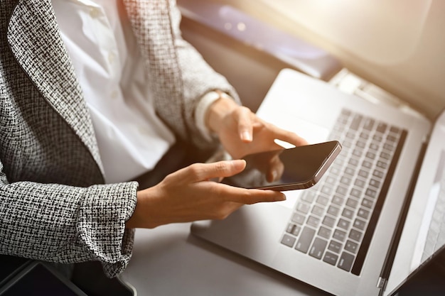 Una donna d'affari che utilizza uno smartphone e un laptop portatile durante il primo piano del volo