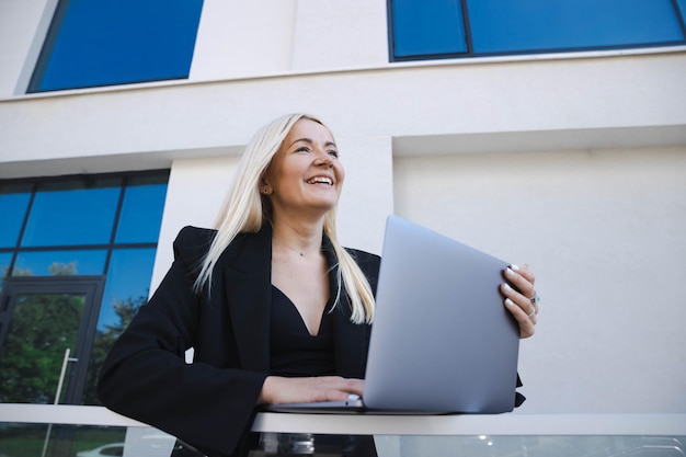 Una donna d'affari con un abito elegante sta lavorando a un laptop per strada