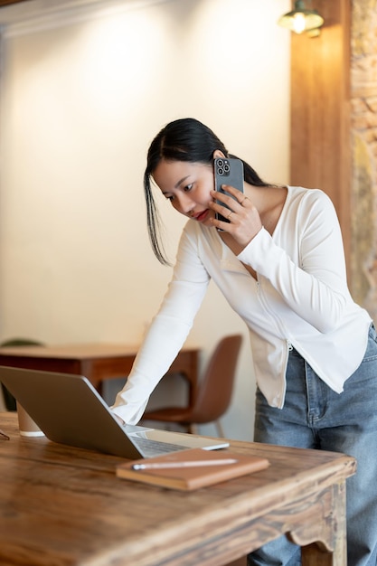 Una donna d'affari concentrata parla al telefono mentre si appoggia e lavora sul suo laptop sul tavolo