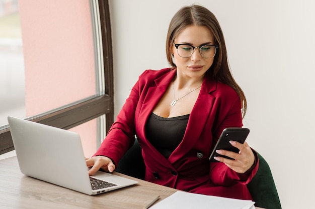 Una donna d'affari di successo vestita di giacca rossa sta lavorando con un laptop in ufficio