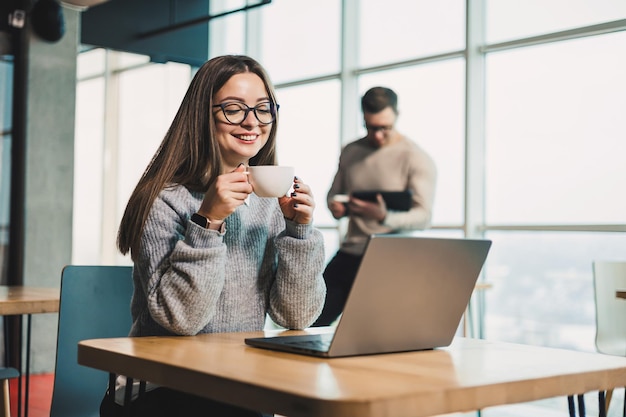 Una donna d'affari freelance sorridente che lavora a un nuovo progetto sul portatile Il concetto di lavoro delle persone d'affare Un moderno ufficio caffè per il lavoro remoto e online con Internet