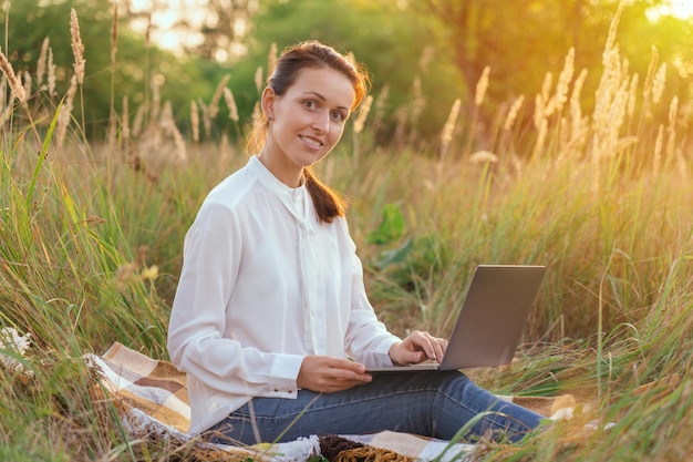 Una donna d'affari gestisce in remoto un reparto seduta in un parco con un laptop in grembo