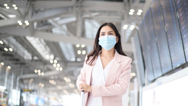 Una donna d'affari indossa una maschera protettiva in aeroporto internazionale, viaggi sotto pandemia Covid-19, viaggi di sicurezza, protocollo di allontanamento sociale, nuovo concetto di viaggio normale