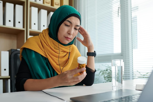 Una donna d'affari musulmana stressata e depressa che guarda un contenitore di pillole.