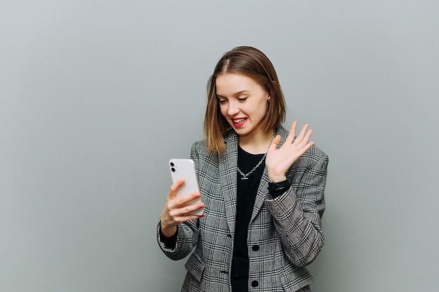 Una donna d'affari positiva in abiti formali scivola su uno smartphone su uno sfondo di un muro grigio