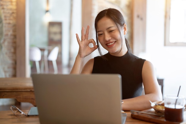 Una donna d'affari si unisce a una riunione online mostrando il cartello "Ok" con la mano che lavora in un bar