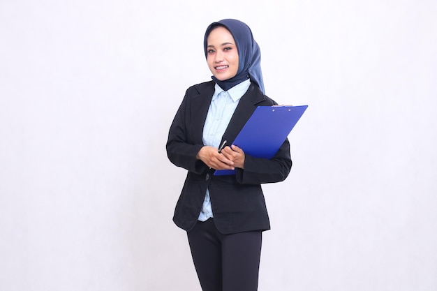 Una donna d'ufficio asiatica matura che indossa un hijab si trova sorridendo allegramente alla telecamera con una penna in mano e