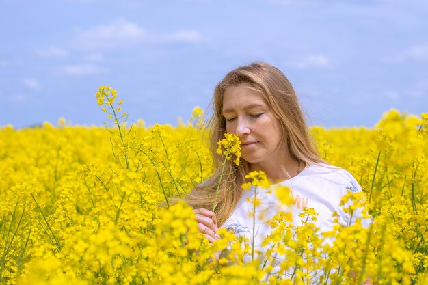 Una donna dai capelli biondi odora profumati fiori gialli in un campo di colza