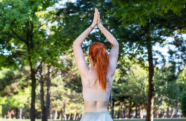 Una donna dai capelli rossi con la pelle chiara che pratica yoga e meditazione nella foresta