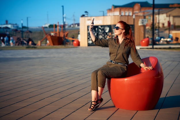 Una donna dai capelli rossi si fa un selfie sul suo smartphone la sera nel parco.