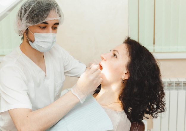 Una donna dai capelli scuri positiva si siede nell'ufficio del dentista durante un dentista di controllo che esamina i denti della donna