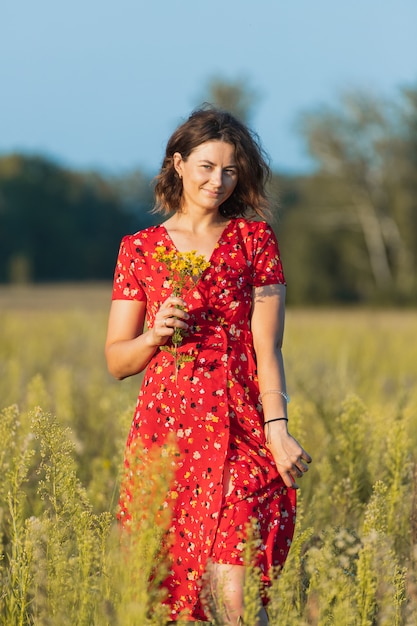 Una donna dai capelli scuri sorride, cammina lungo il campo verde vestita di abito rosso