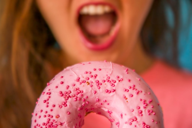 Una donna dalle labbra rosa tiene in mano una ciambella rosa con dei granelli sopra.