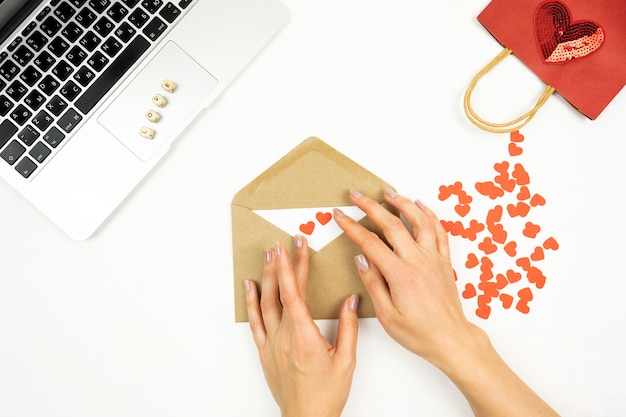 Una donna decora una busta marrone con cuori rossi per il giorno di San Valentino