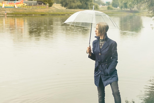 Una donna di 3040 anni con un mantello blu va sotto un ombrello trasparente nel parco