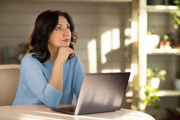 Una donna di 35 anni con una giacca blu seduta al computer e guardando malinconicamente di lato