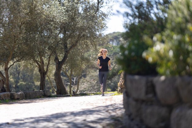 Una donna di forma fisica sorridente adulta che fa jogging nel parco verde