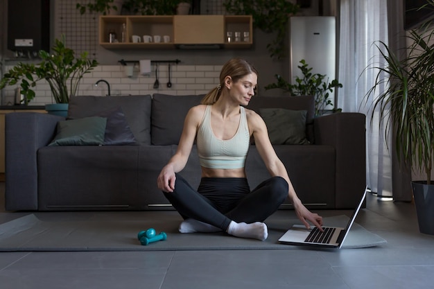 Una donna di mezza età a casa impegnata in fitness e nebbia usa un laptop per attività di gruppo online