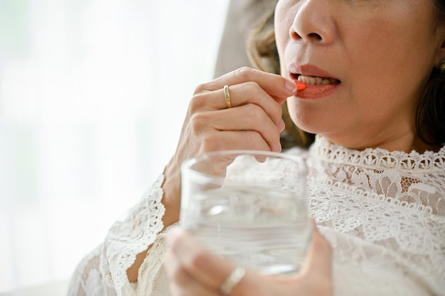 Una donna di mezza età asiatica malata che prende un'immagine del primo piano della capsula della medicina o della vitamina