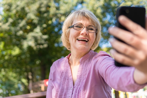 Una donna di mezza età che parla al telefono e si fa un selfie. Una donna comunica, blogga, controlla la posta elettronica. Social network, rete.