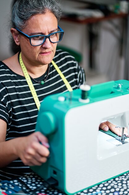 Una donna di mezza età con i capelli bianchi cuce con la macchina da cucire a casa.