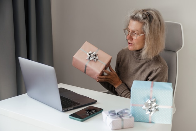Una donna di mezza età prepara i regali di Natale per i suoi parenti e comunica con loro tramite video