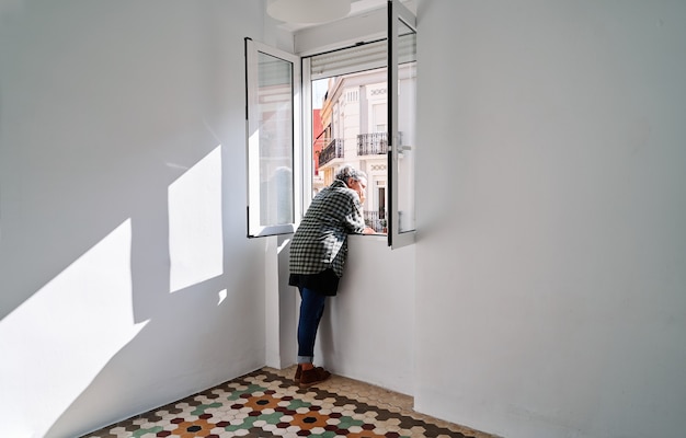 Una donna di mezza età si affaccia alla finestra in una stanza con pavimento idraulico colorato
