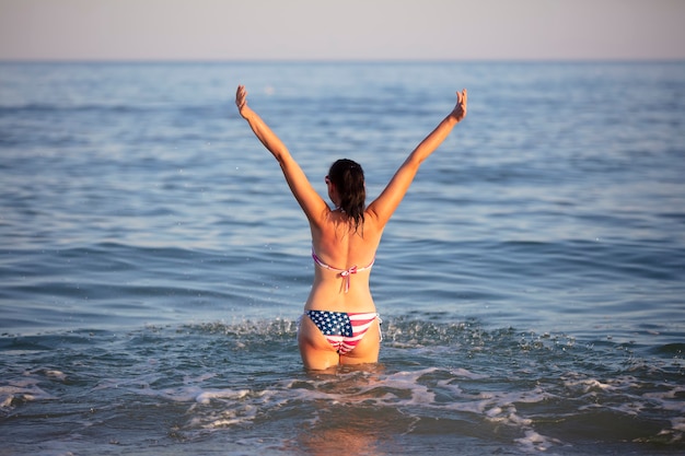 Una donna di mezza età sta nell'acqua di mare con le braccia alzate in costume da bagno