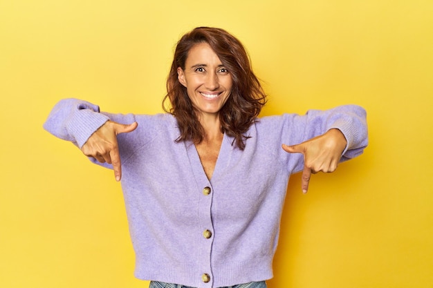 Una donna di mezza età su uno sfondo giallo punta verso il basso con le dita sensazione positiva